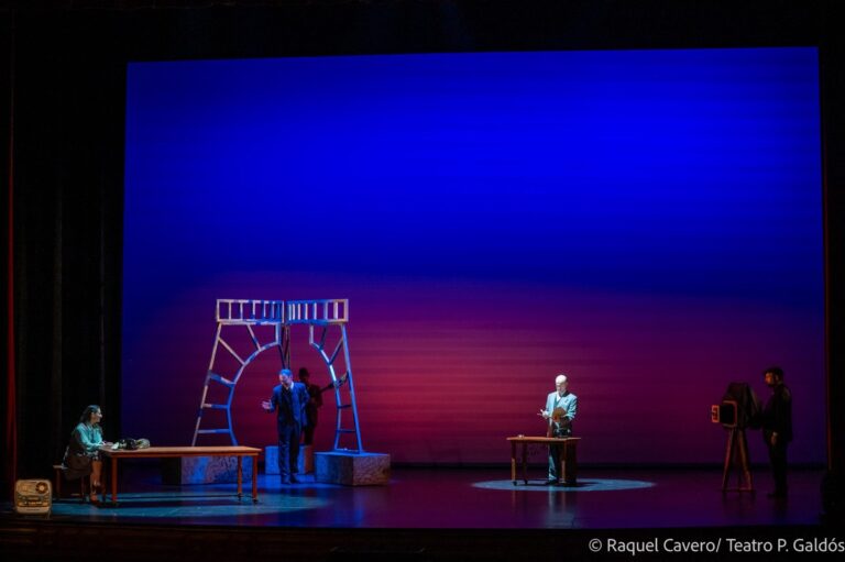 Plano general del escenario con la escenografía de estructuras dibujadas a trazos, entre luz azul y roja. Foto: Raquel Cavero / Teatro Pérez Galdós