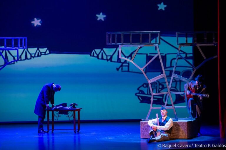 Escena nocturna con estrellas proyectadas, un intérprete sentado sobre un bloque de piedra y otro inclinado sobre la mesa. Foto: Raquel Cavero / Teatro Pérez Galdós