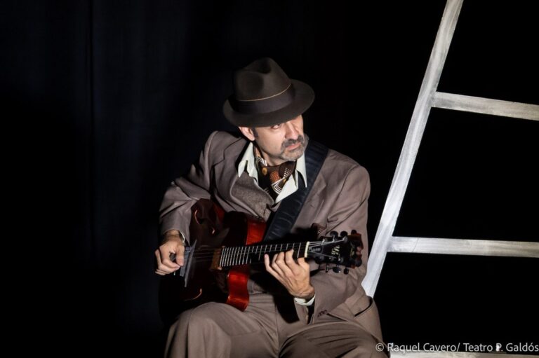 Yul Ballesteros toca la guitarra en directo, con sombrero, junto a una escalera de la escenografía. Foto: Raquel Cavero / Teatro Pérez Galdós