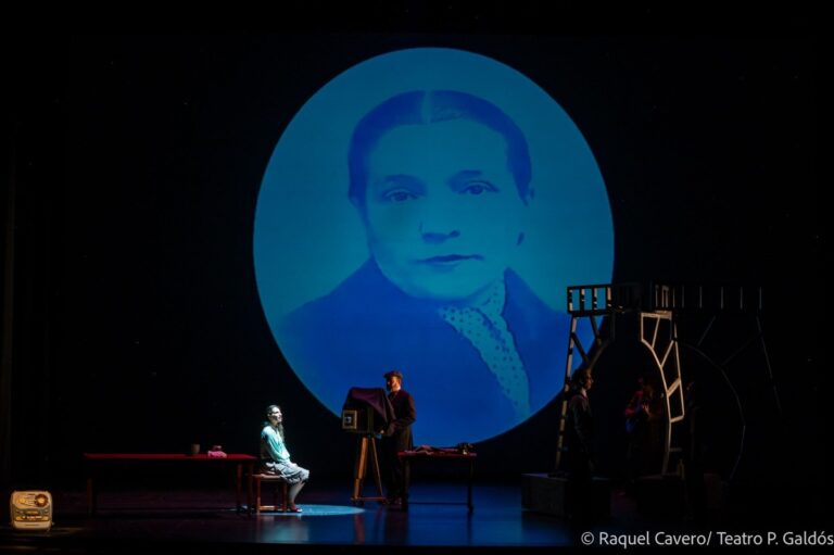Retrato fotografico antiguo proyectado en un círculo azul, con un intérprete sentado a la mesa debajo. Foto: Raquel Cavero / Teatro Pérez Galdós