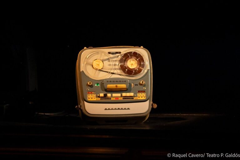 Primer plano del magnetófono de bobinas que acompaña la acción, iluminado sobre fondo negro. Foto: Raquel Cavero / Teatro Pérez Galdós