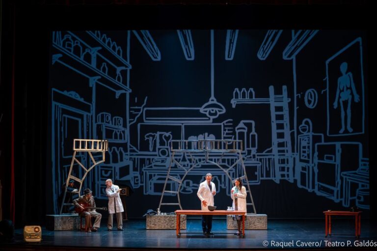 Escenografía que dibuja un laboratorio, con tres intérpretes de bata blanca alrededor de la mesa. Foto: Raquel Cavero / Teatro Pérez Galdós