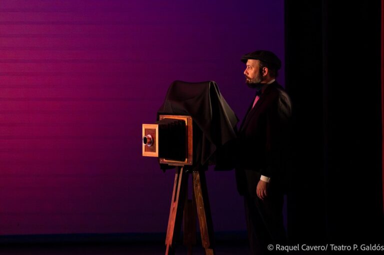 Un personaje junto a una cámara fotografica de fuelle, bajo luz malva. Foto: Raquel Cavero / Teatro Pérez Galdós
