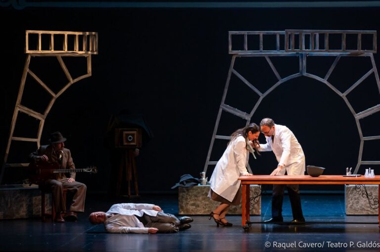 Escena de laboratorio: dos intérpretes de bata sobre la mesa y un cuerpo tendido en el suelo. Foto: Raquel Cavero / Teatro Pérez Galdós