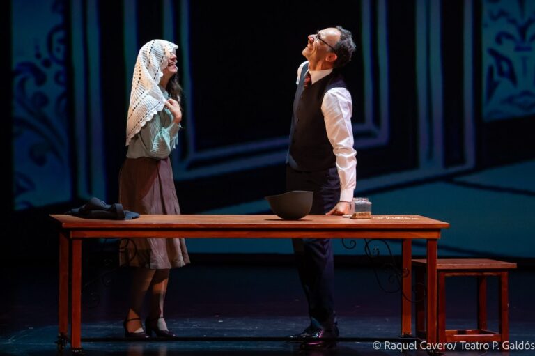 Dos intérpretes de pie a ambos lados de la mesa larga, ante la escenografía dibujada. Foto: Raquel Cavero / Teatro Pérez Galdós