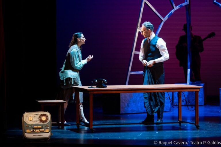 Dos intérpretes conversan junto a la mesa, con el magnetófono de bobinas en primer término. Foto: Raquel Cavero / Teatro Pérez Galdós