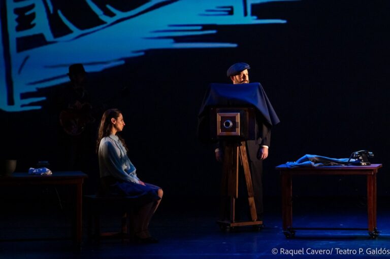 Una intérprete sentada posa ante la cámara de fuelle que maneja un personaje cubierto por el paño. Foto: Raquel Cavero / Teatro Pérez Galdós