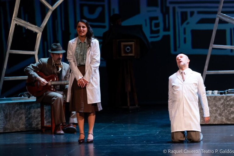 El guitarrista sentado, una intérprete de bata y un tercer personaje de rodillas con los brazos abiertos. Foto: Raquel Cavero / Teatro Pérez Galdós