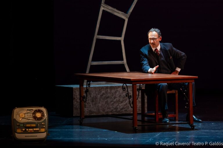 Un intérprete sentado al escritorio, con el magnetófono de bobinas en primer término. Foto: Raquel Cavero / Teatro Pérez Galdós